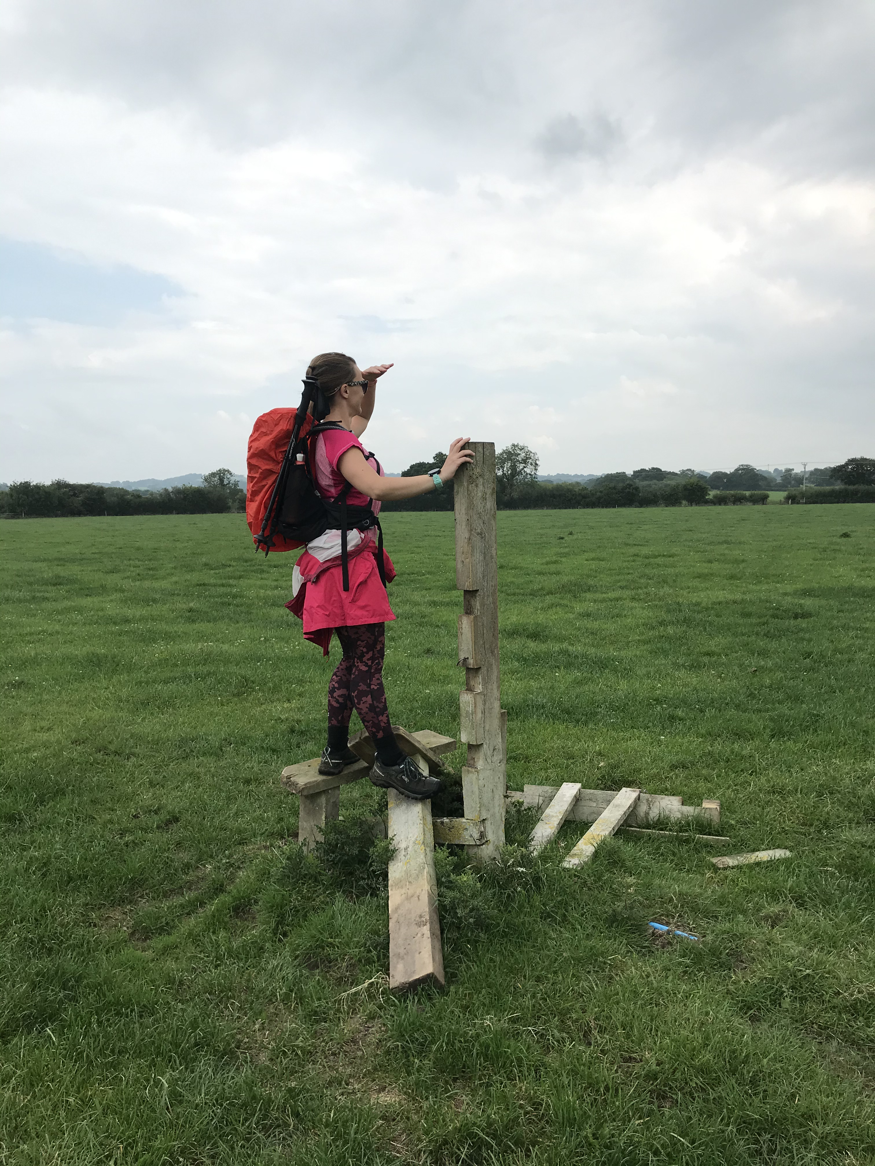 A woman in walking kit standing on a stile with no fencing